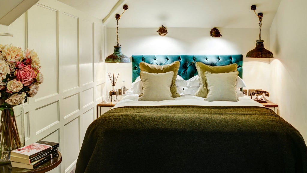 Luxurious cosy hotel room with plush white bedding, soft neutral tones, elegant wooden furniture, and warm ambient lighting in a charming UK boutique setting