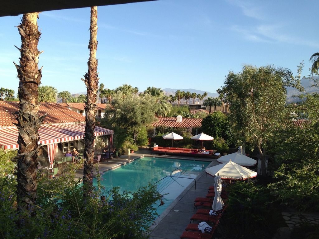 Spanish colonial-style luxury hotel exterior with white stucco walls, red tile roof, manicured palm trees and desert landscaping at sunset