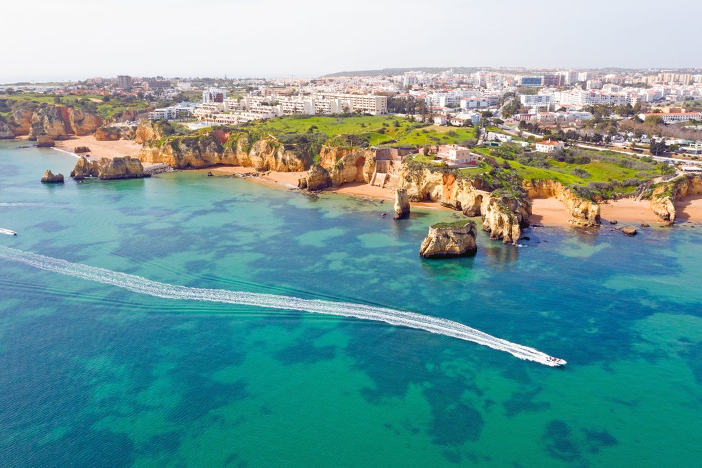 Sleek white catamaran anchored in crystal-clear turquoise waters near a pristine Portuguese beach with dramatic coastal cliffs