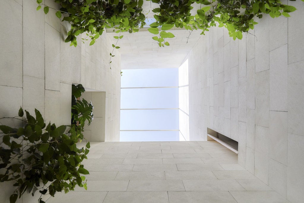 Minimalist luxury hotel courtyard in Mexico City with geometric stone architecture, lush green plants, and soft natural lighting creating serene urban sanctuary