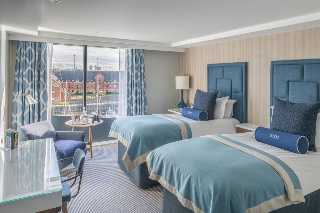 Twin hotel room with city view, plush white bedding, modern furnishings, and large window overlooking Southampton's scenic harbour landscape