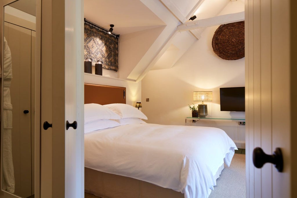 Elegant bedroom at Grove of Narberth with plush white bedding, soft neutral tones, vintage furnishings, and warm natural light filtering through delicate curtains