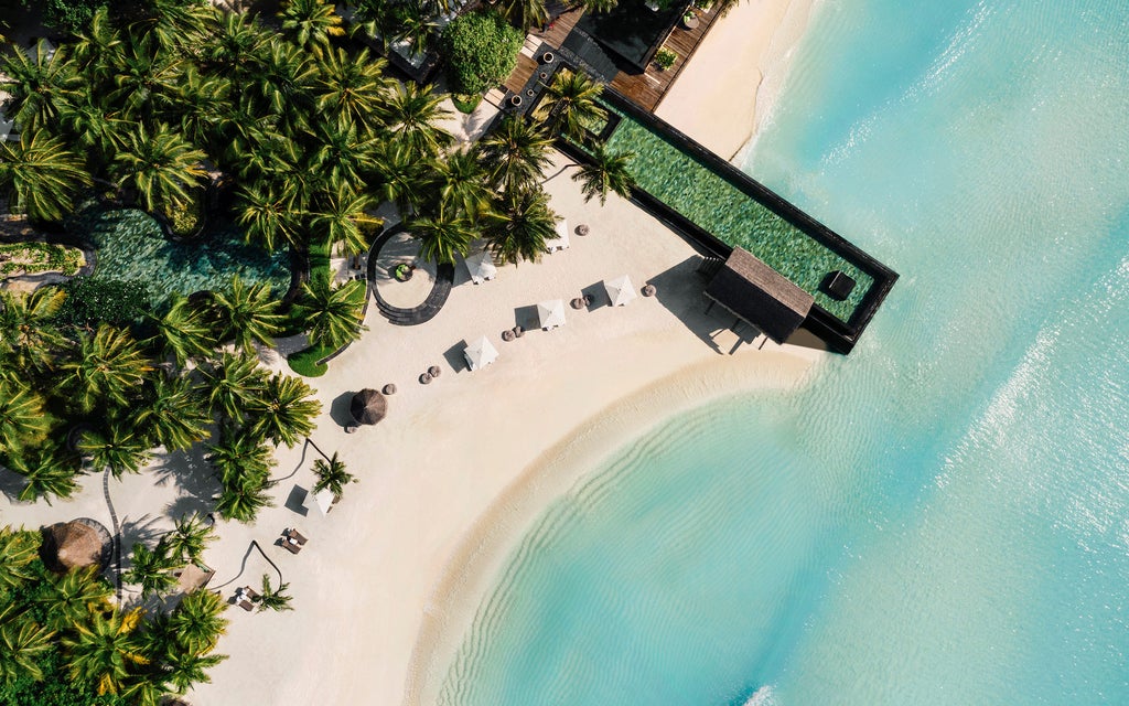 Luxurious overwater villa with infinity pool overlooking turquoise Maldivian lagoon, surrounded by palm trees and pristine beach