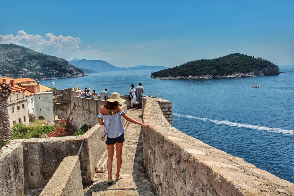 Cobblestone streets of Dubrovnik's Old Town with ancient stone buildings, ornate archways, and local shops under clear blue sky