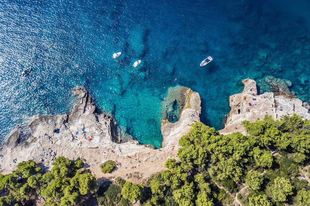 Dramatic aerial view of Dubrovnik's ancient stone walls and red-tiled roofs along crystal-clear Adriatic Sea at golden hour