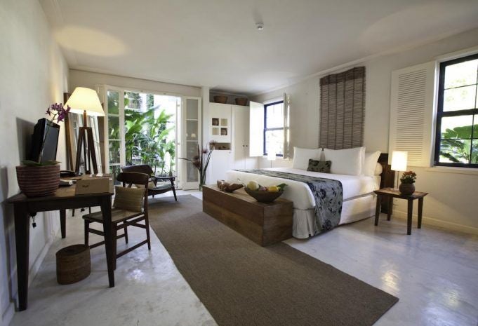 Elegant deluxe hotel room with rich wood furnishings, plush white bedding, and warm Brazilian-inspired decor in historic Santa Teresa neighborhood of Rio de Janeiro