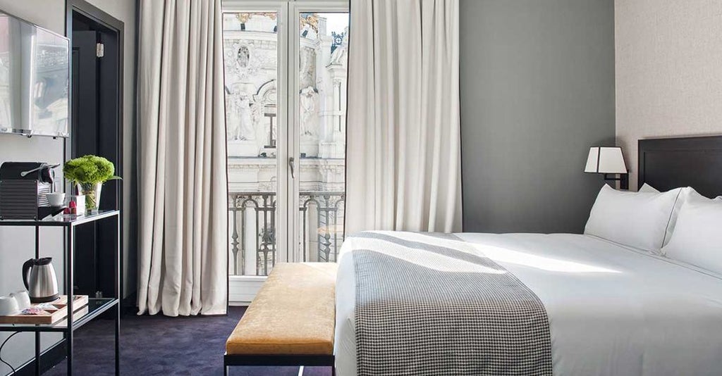 Elegant deluxe hotel room with panoramic city views of Madrid, featuring modern minimalist decor, plush white bedding, and large windows showcasing urban skyline