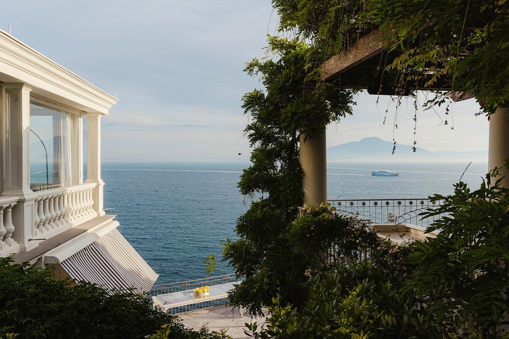 Luxurious historic hotel perched on Sorrento's cliffside with elegant white facade, blue Mediterranean waters, and lush coastal landscape below