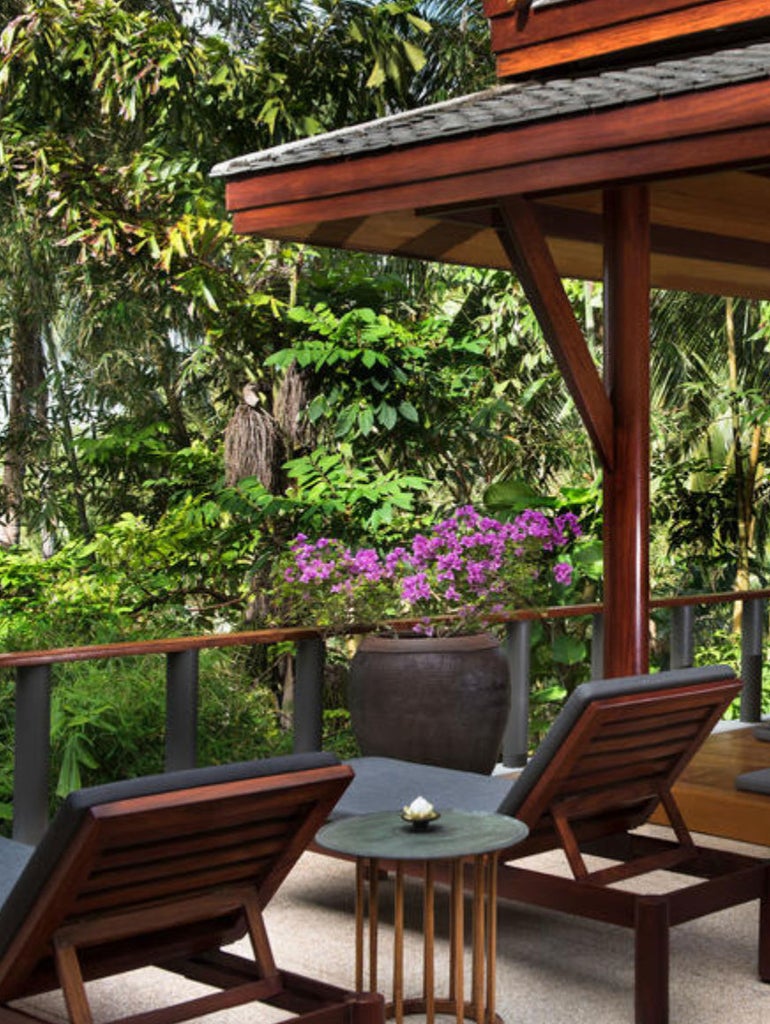 Elegant pavilion bedroom with floor-to-ceiling windows, teak furniture, white linens, overlooking private pool and lush Thai gardens