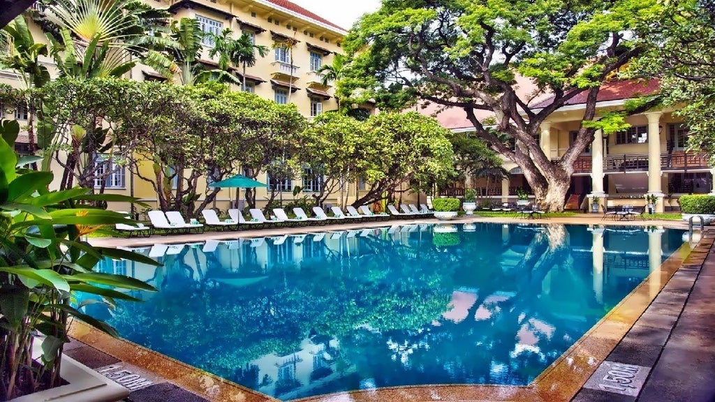 Grand colonial-style Raffles Hotel with white facade, elegant palm-lined driveway, manicured gardens and vintage Mercedes parked outside