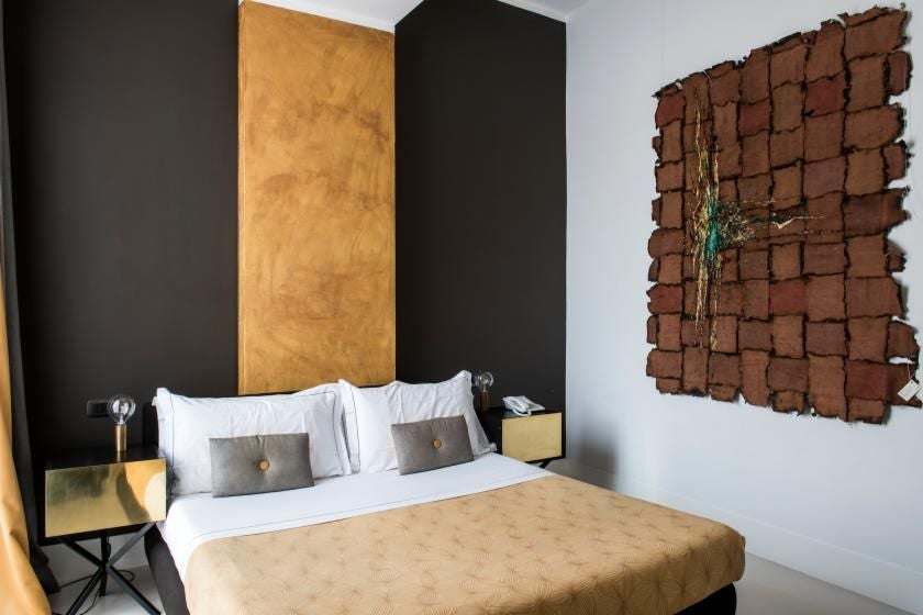 Elegant modern hotel room with soft neutral tones, plush white bedding, minimalist design, and glimpse of roman architectural details near Piazza di Spagna