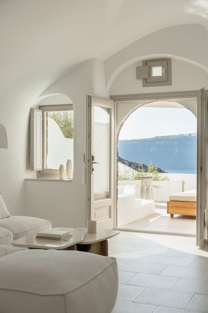 Luxurious white-walled Cycladic-style superior suite with minimalist design, private terrace overlooking azure Aegean Sea in Oia, Santorini