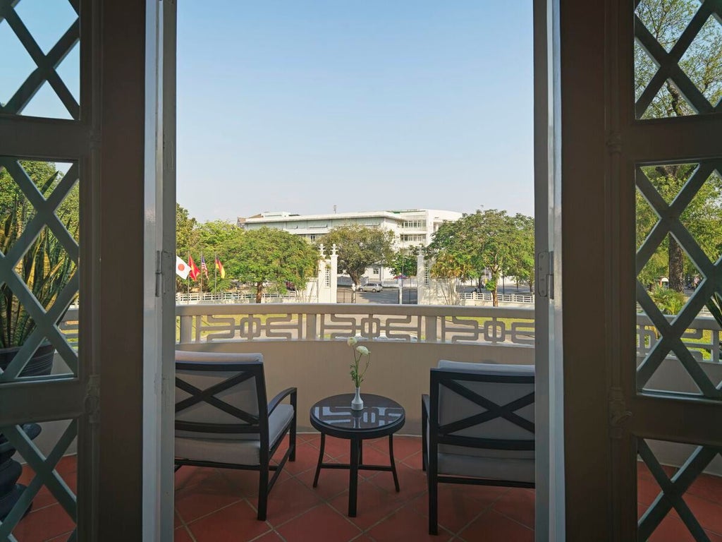 Elegant colonial-style junior suite with plush white bedding, wooden floors, high ceilings, and Vietnamese-inspired decor at luxury boutique hotel in central Vietnam