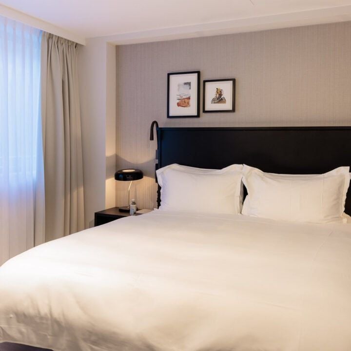 Luxurious king suite with plush white bedding, modern minimalist design, panoramic city view, and sophisticated neutral color palette in Brussels hotel room