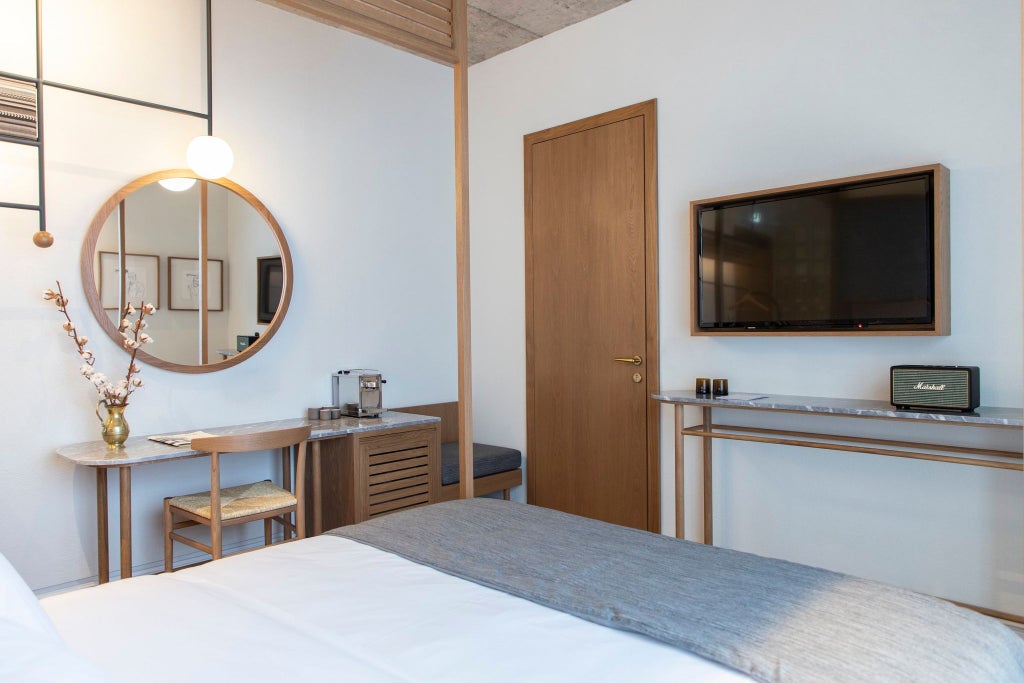 Spacious luxury hotel room with elegant wooden furnishings, plush white bedding, and minimalist design overlooking Athens' historic urban landscape