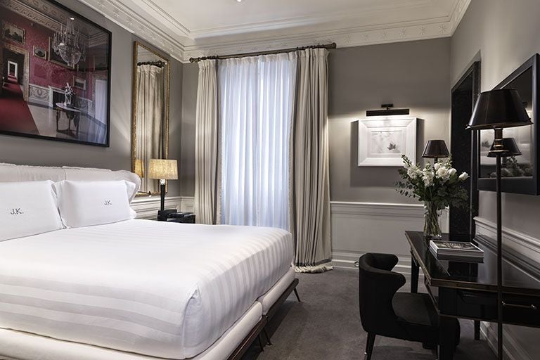 Elegant Italian hotel room with neutral palette, luxurious king bed, plush white linens, marble bathroom, and sophisticated designer furniture in soft tones