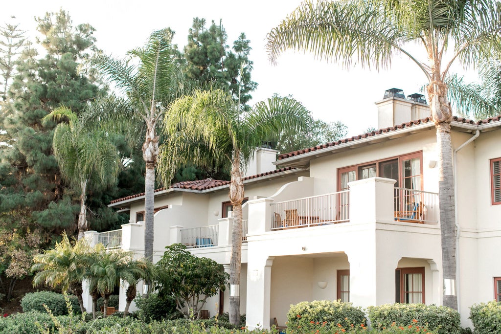 Expansive luxury resort with Mediterranean architecture nestled among rolling hills, featuring lush gardens and palm-lined pool area