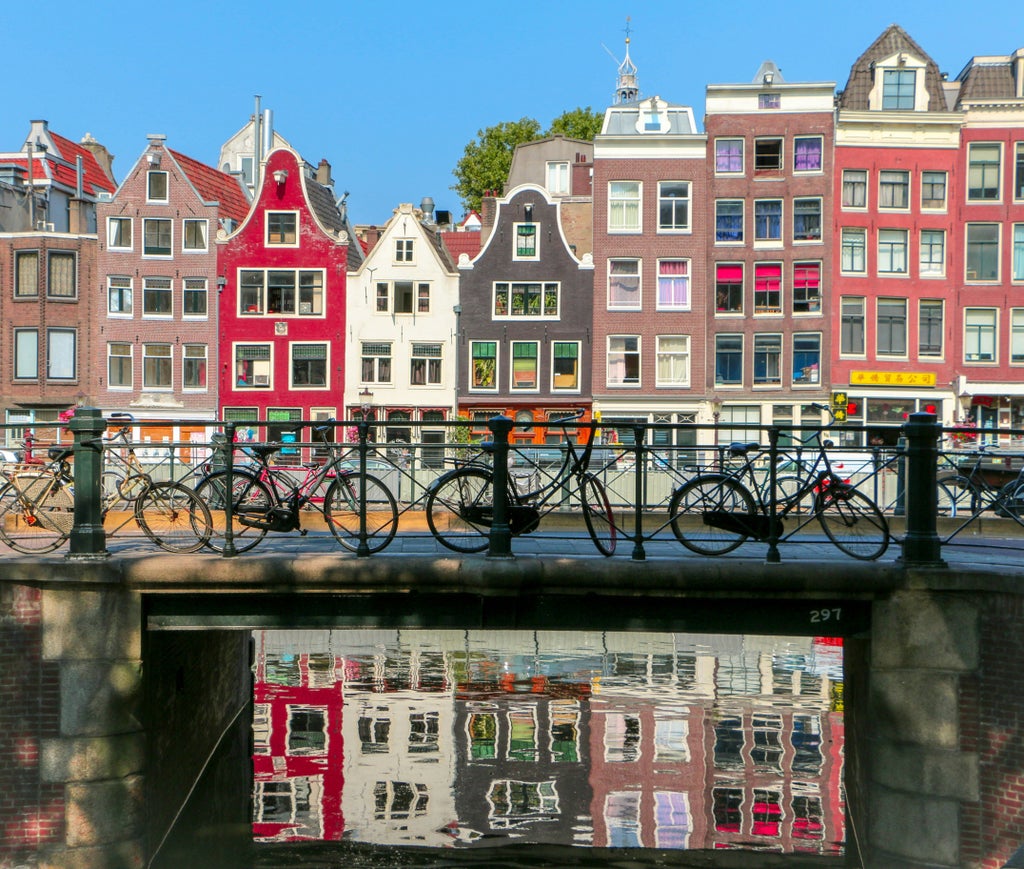 Iconic Amsterdam canal at twilight with vintage bridges, elegant townhouses reflecting in calm waters, and moored boats