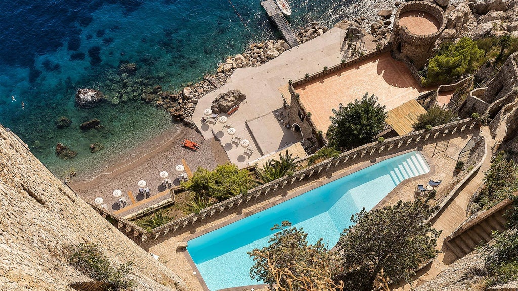 Elegant Italian cliffside hotel with infinity pool overlooking Amalfi Coast, featuring white Mediterranean architecture and terraced gardens