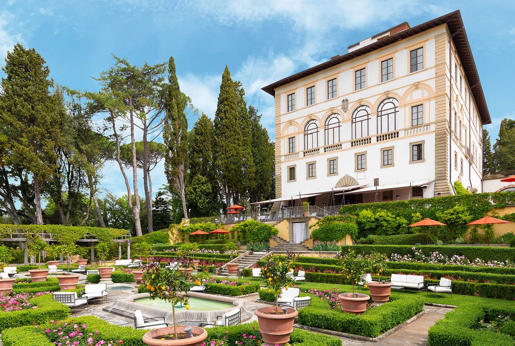 Mediterranean luxury hotel nestled on Tuscan hillside with manicured gardens, grand facade, and panoramic views over Florence below