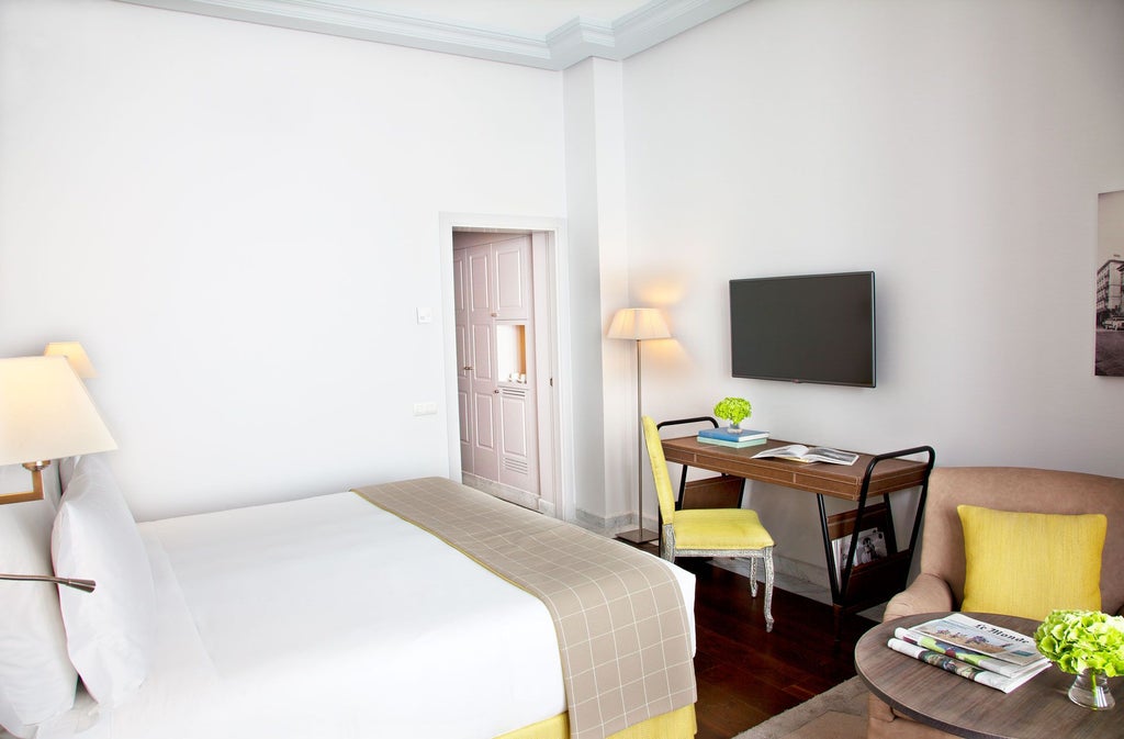 Elegant Spanish hotel room with plush white bedding, warm wooden furniture, soft lighting, and chic modern decor in neutral tones at URSO Hotel & Spa