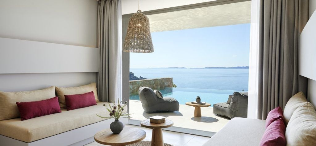 Luxurious deluxe hotel room with panoramic Aegean Sea view, featuring modern minimalist design, crisp white linens, and sleek contemporary furnishings.