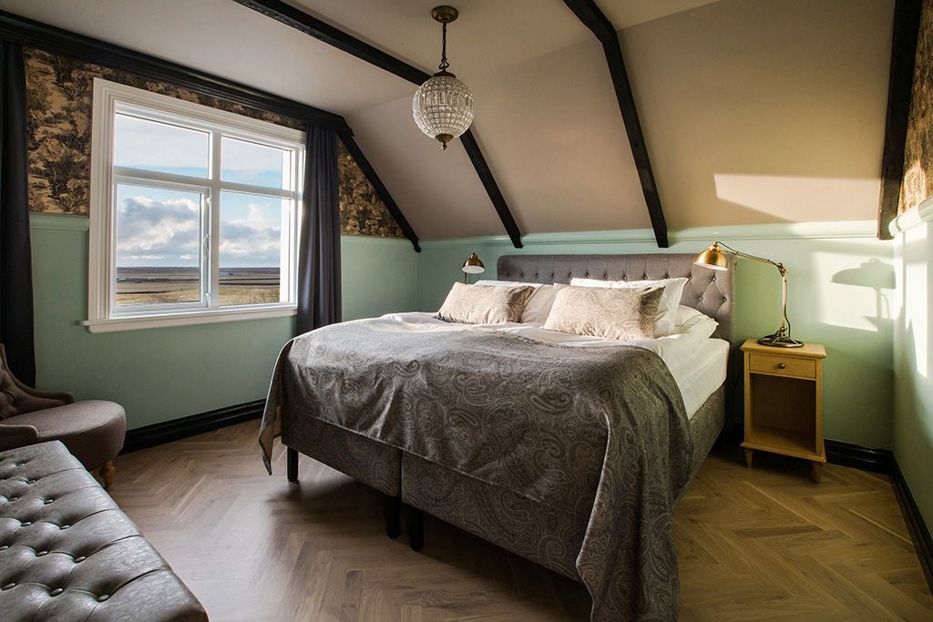 Luxurious mini suite at Skálakot Manor Hotel, Iceland, featuring elegant wooden furnishings, plush bedding, and panoramic mountain landscape through large windows