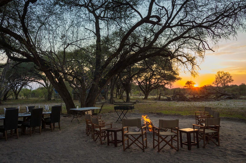 Luxurious safari tent overlooking Botswana wilderness at sunset, with private deck, canvas walls and thatched roof amid acacia trees