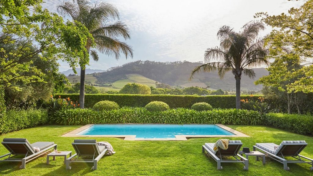 Elegant South African luxury villa with stone facade, infinity pool overlooking vineyards, and modern outdoor lounge under mountains