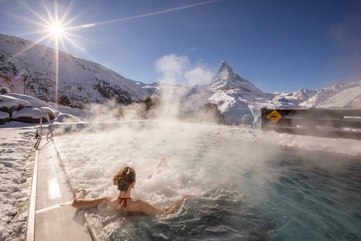 Five-star mountain lodge with stone and wood facade nestled in snowy Swiss Alps, panoramic Matterhorn views, luxury terrace dining