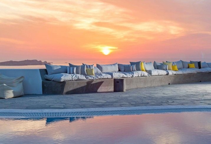 Elegant whitewashed boutique hotel with minimalist Cycladic architecture, infinity pool overlooking Mykonos coastline at golden hour