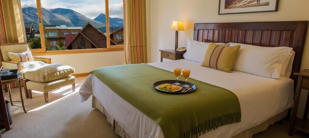 Elegant standard hotel room with plush white bedding, wood floors, and large windows overlooking scenic Ushuaia landscape in Argentina's Los Cauquenes Resort