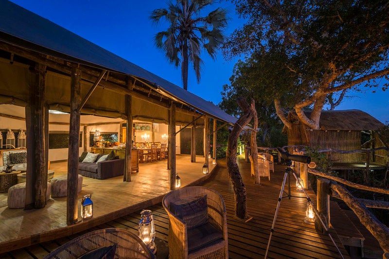 Small luxury safari tent elevated on wooden deck in canopy, overlooking lush Okavango Delta wetlands at sunset through trees