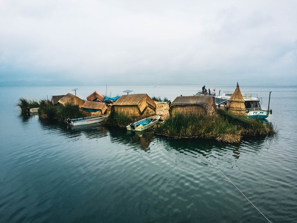 Serene Lake Titicaca reflecting snow-capped Andes mountains, with traditional reed boats docked at a floating Uros island at sunset