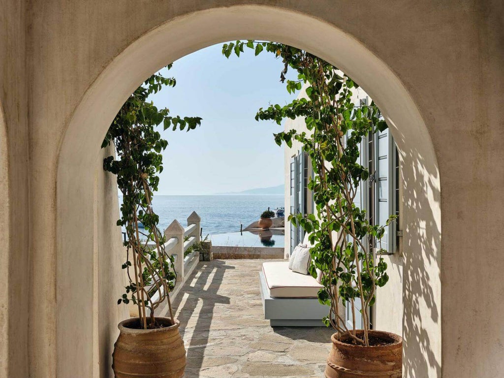 Luxurious white Cycladic hotel building with infinity pool overlooking Mykonos coastline, featuring curved balconies and ocean views