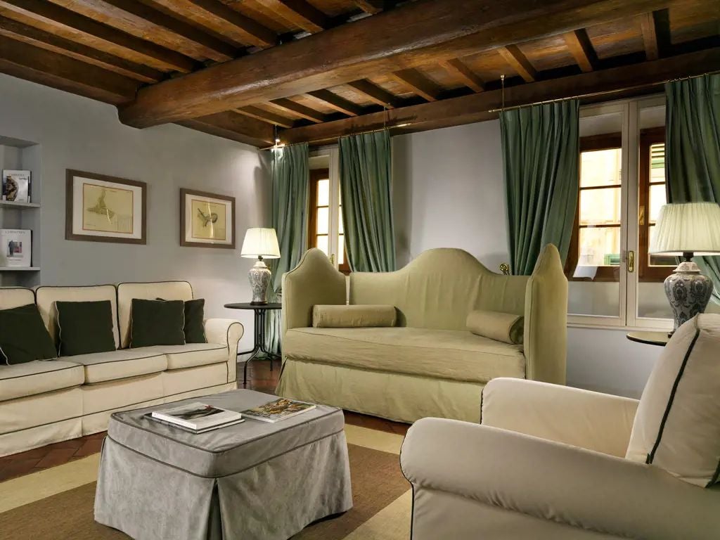 Elegant historic Florentine studio with ornate frescoed ceiling, antique furnishings, and large windows overlooking a Renaissance palace courtyard.