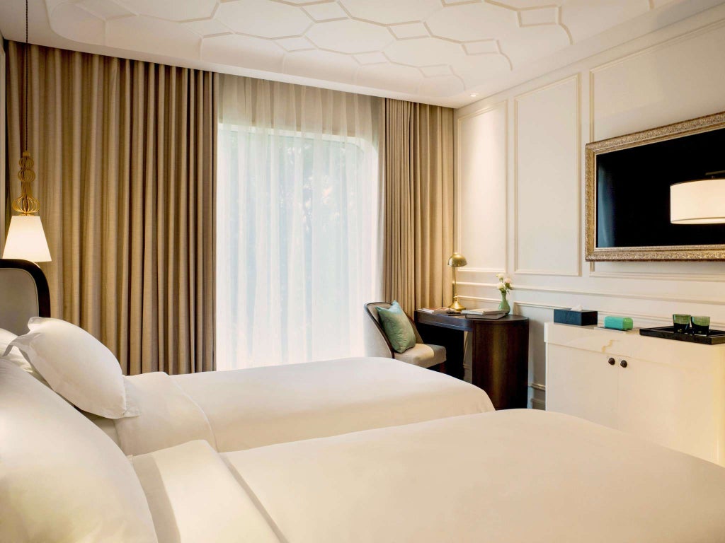 Elegant hotel room with two single beds, floor-to-ceiling windows overlooking Saigon cityscape, modern decor with Vietnamese accents