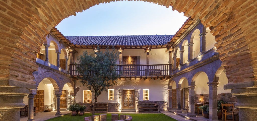 Elegant colonial courtyard of historic boutique hotel with stone archways, terracotta floors, and potted plants in Cusco, Peru