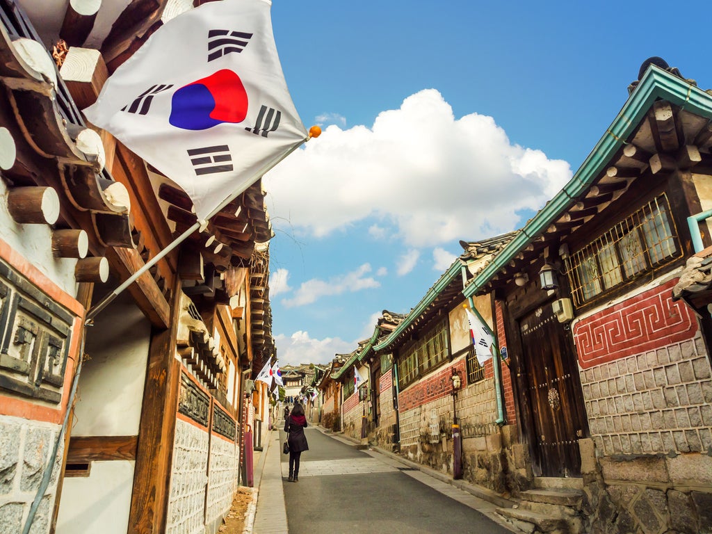 Young woman in traditional hanbok dress strolls through ornate palace courtyard with elegant roof details in Jeonju Hanok Village