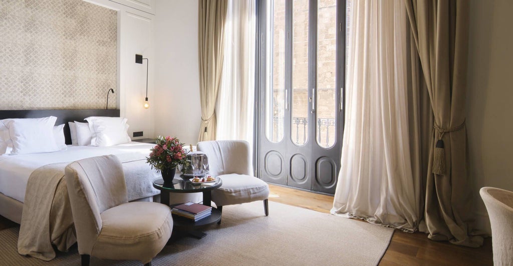 Elegant junior suite with minimalist design, warm wooden floors, plush white bedding, and large windows overlooking historic Sant Francesc square in Palma