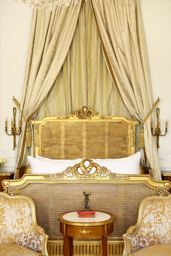 Elegant corner king bedroom in French château featuring ornate crown molding, crystal chandelier, and sweeping countryside views