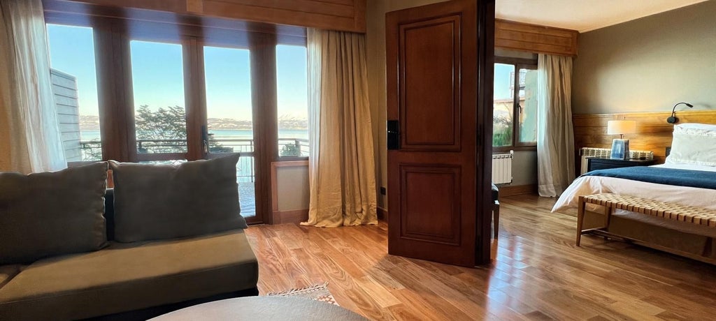 Luxurious senior suite overlooking Beagle Channel, featuring elegant decor, floor-to-ceiling windows, and panoramic views of Argentinian mountainous landscape