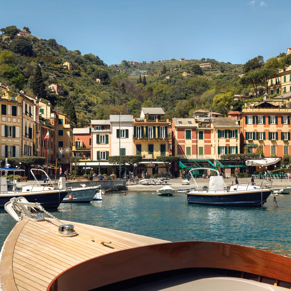 Colorful row of luxury Italian villas along Portofino's harbor, with boats moored in turquoise Mediterranean waters at sunset.