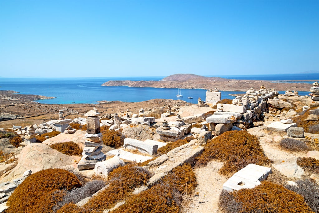 Whitewashed Greek villas with blue domes cascade down Mykonos hillside, overlooking turquoise Aegean Sea at golden sunset