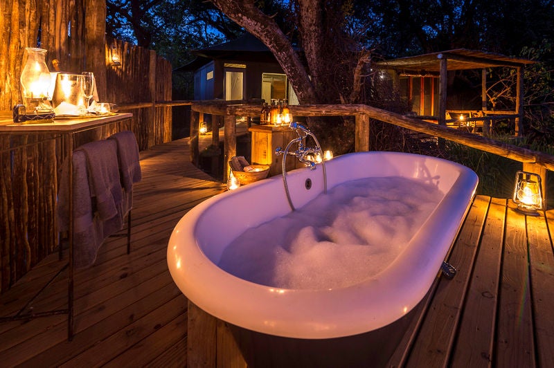 A luxurious safari lodge with tented suites on elevated wooden platforms, nestled among palm trees overlooking the Okavango Delta waters