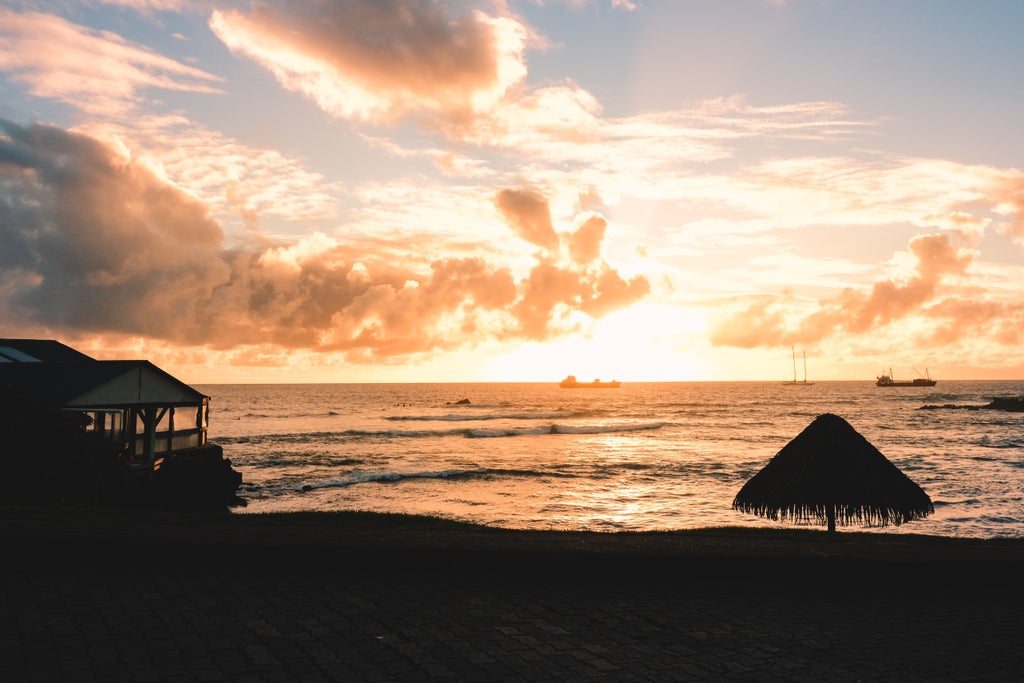 Easter Island's iconic moai statues stand silently at sunset, with golden sky and rugged coastline dotted with scattered palm trees