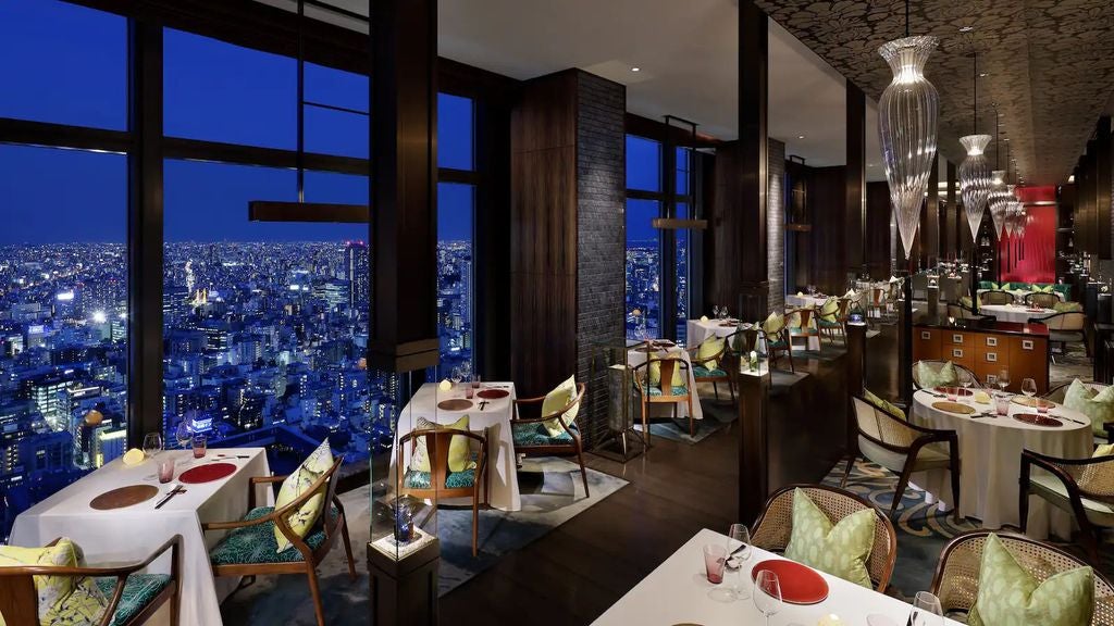 Elegant high-rise Mandarin Oriental hotel in Tokyo with floor-to-ceiling windows, illuminated at night against city skyline backdrop