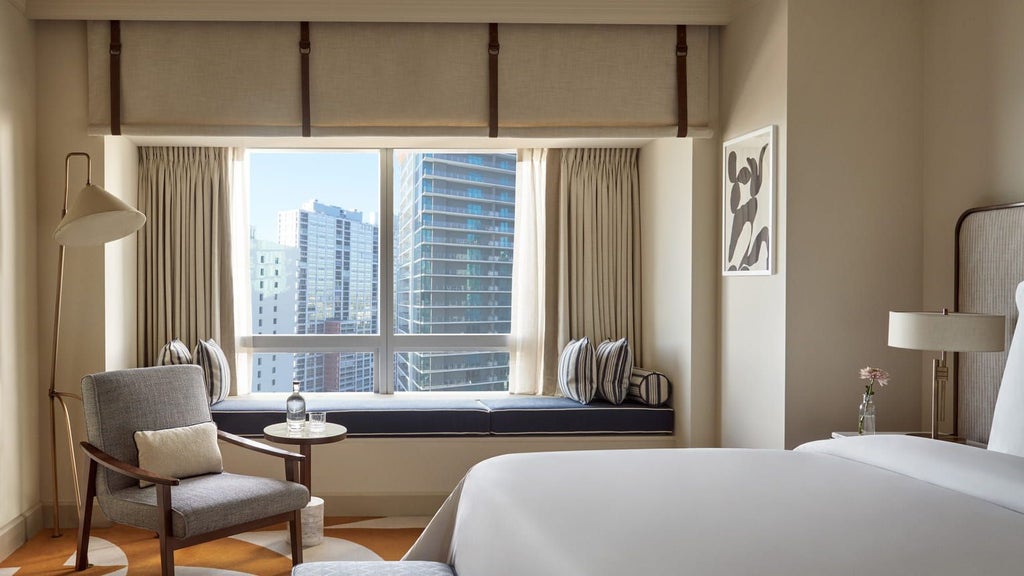 Spacious corner suite with panoramic views of Miami's skyline, featuring modern decor, floor-to-ceiling windows, and elegant four-poster bed overlooking Biscayne Bay