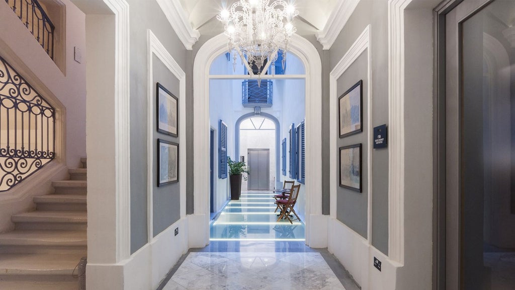 Stunning boutique hotel facade in Malta with elegant white stone exterior, arched windows, and warm Mediterranean lighting at dusk