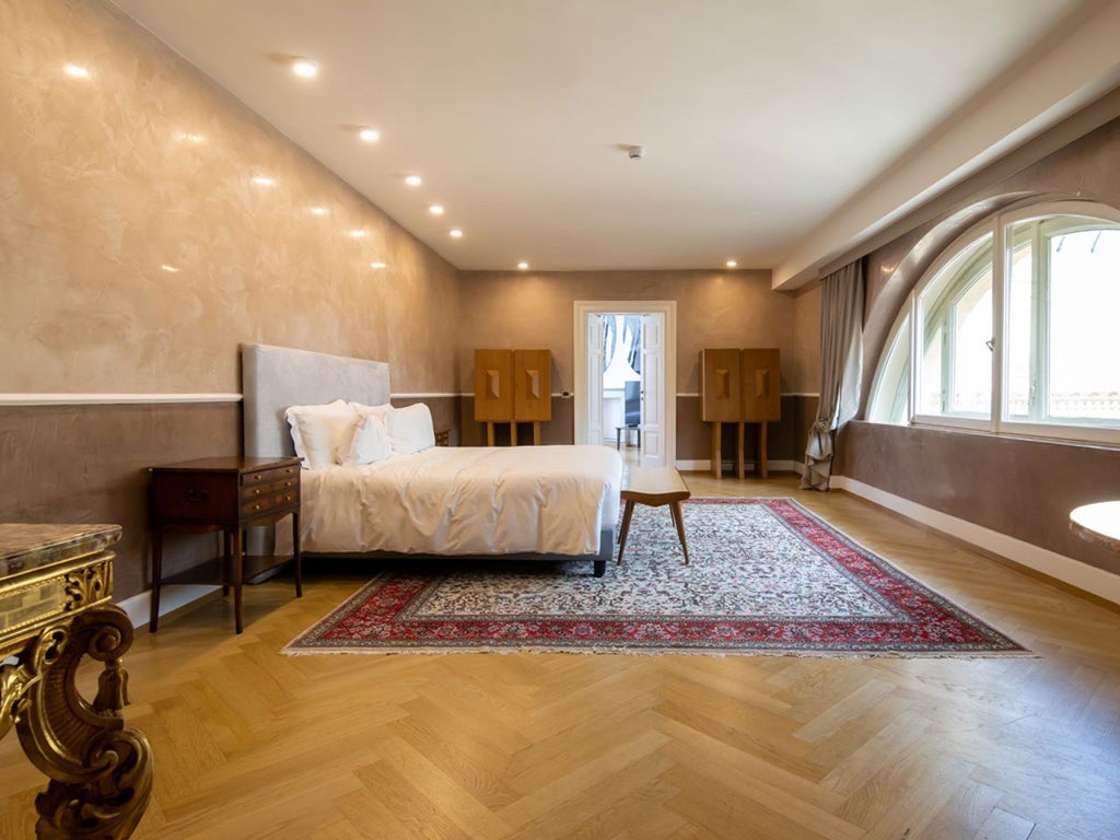 Elegant deluxe hotel room with modern Italian design, large windows showcasing urban scenery, luxurious white bedding, and sleek minimalist furnishings